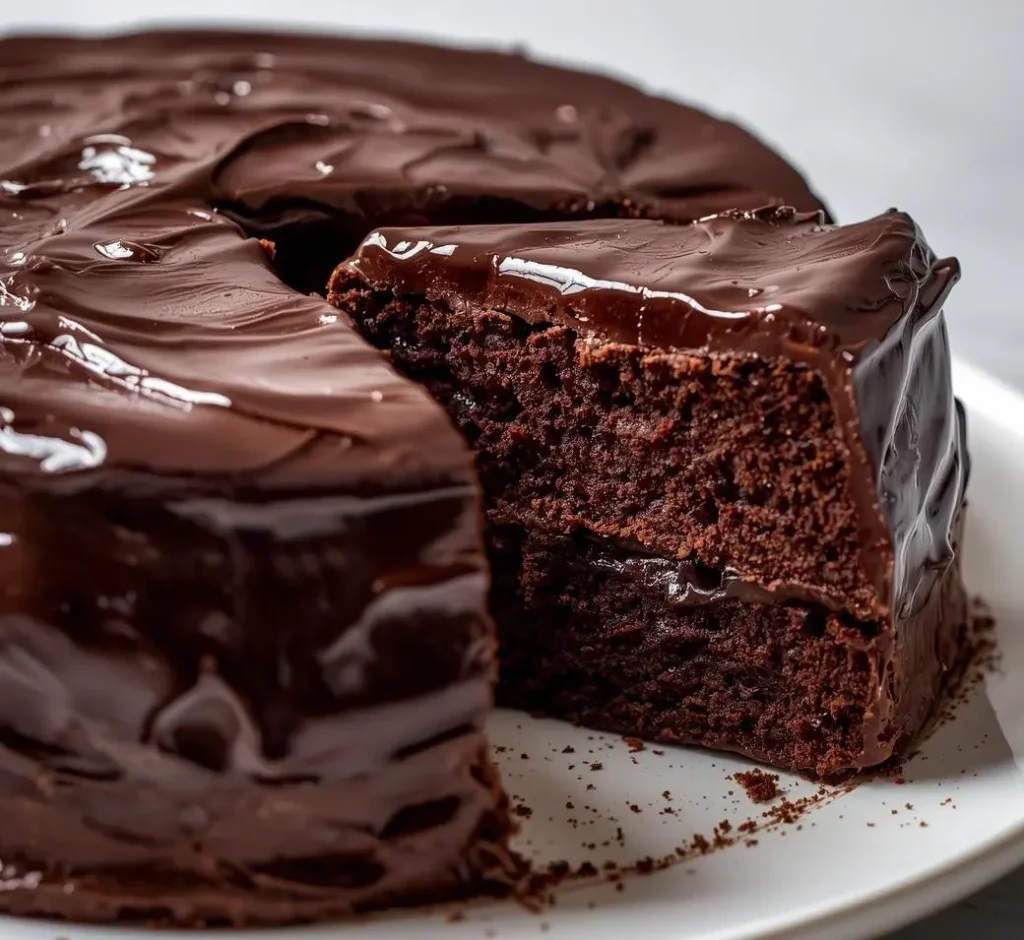 Rich and moist Chocolate Fudge Cake topped with glossy chocolate ganache and sliced on a plate